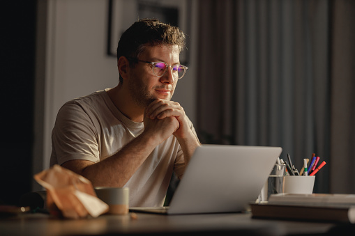 The image shows a middle-aged Caucasian man with eyewear, deeply focused on work from his home environment. He is comfortably using a laptop, embodying the modern work-from-home setup. The setting suggests a blend of professionalism and the personal comfort of being in one's own space, highlighting the increasingly common remote working lifestyle.