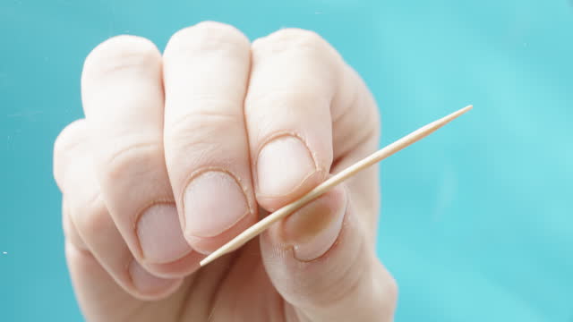 Wooden toothpick on a blue background, a hand picks it up from a glass transparent table. View from below.