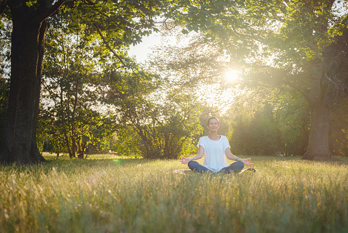 Young asian woman doing meditation in morning or evening at park, healthy woman relaxing and practicing yoga at city park. Mindfulness, destress, Healthy habits and balance concept
