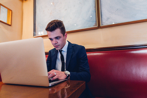 Candid image of a young man wearing suite and tie participating in a job interview remotely via a laptop through a video call.