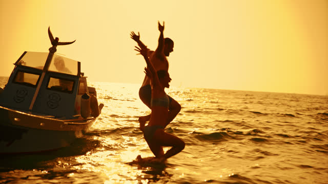 Carefree Couple Jumping Into Sea Water From Boat During Sunset