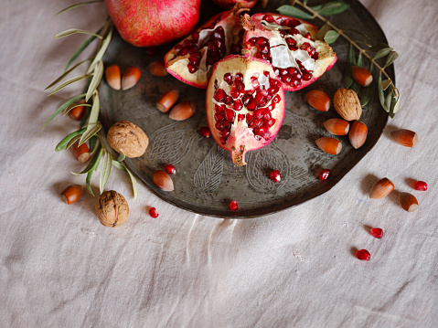 Image of Still Life with Turkish Pomegranate and olive branch on old retro plate. Dark wood background, antique copper plate. Fresh ripe whole pomegranates, opened pomegranate and seeds