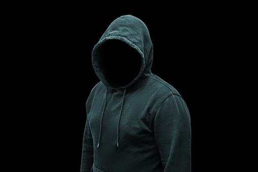 Mysterious faceless hooded anonymous criminal, silhouette of computer hacker, cyber terrorist or gangster on black background.