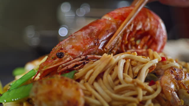 Person placing a prawn on top of stir fried noodles