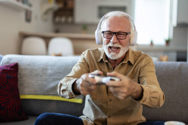 istock Bearded senior man with gamepad playing video game at home. Elderly man with gamepad playing video game in the living room during the day. 1889520854