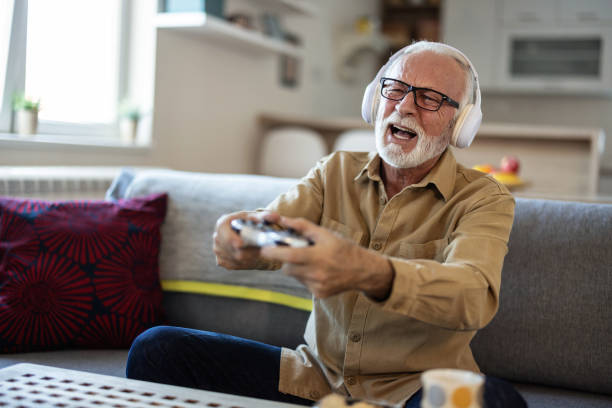 istock Excited senior man looking at tv screen and holding controller while playing video game at home in living room. 1889521366