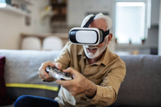 istock Senior man playing video game using virtual reality goggles at home. Senior man on couch, playing a VR game. 1889530134