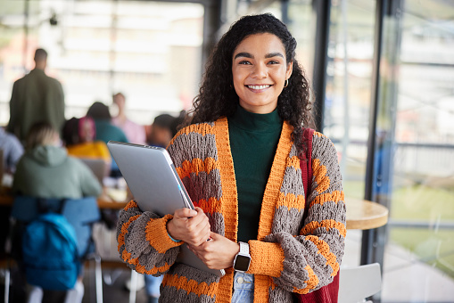 Portrait of a smiling young female college student standing with her laptop in a cafeteria at school