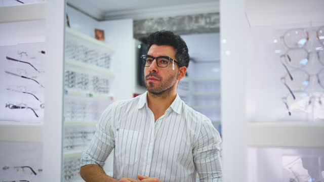 Optician helping a client choose glasses during his optometry appointment. male customer in consult with optometrist, fitting on a pair of eyewear spectacles for vision corrections or better eyesight