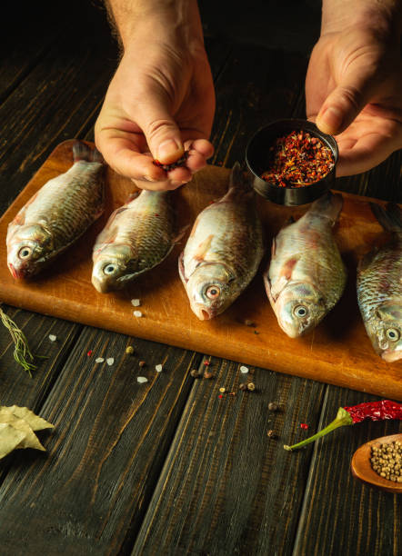 istock Cooking marinated fish with aromatic spices by the hands of a chef on a cutting board. Concept of cooking crucian fish on the kitchen table 1889559123
