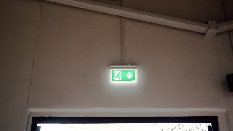 Green emergency exit sign on the wall above the door, down arrow and running person pointing the right direction to escape in case of danger, emergency exit symbol, direction for evacuation