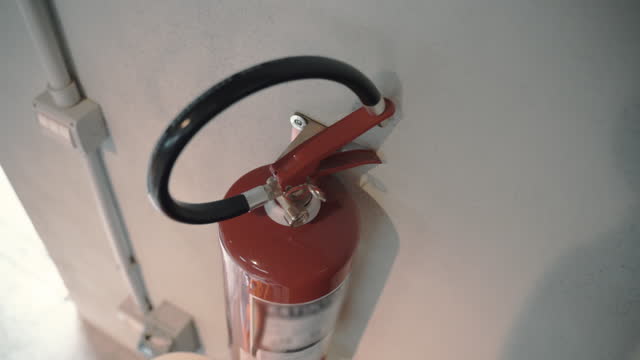 Fire extinguisher hanging on white wall inside the building to be used in case of emergency, obligatory equipment on industrial factories and other public institutions in case of fire danger, portable fire extinguisher inspection