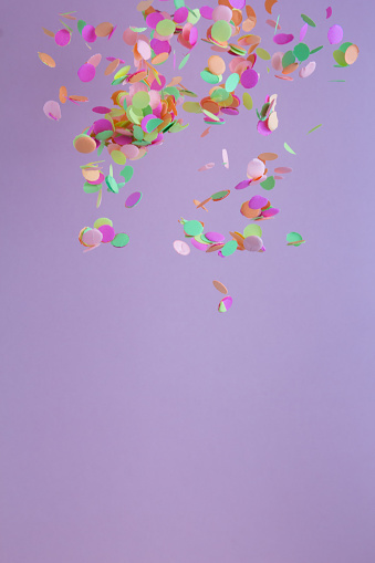 Colorful confetti falling, abstract. Warm colors: pink, yellow and orange. Carnival party background concept, space for text. Vertical orientation.