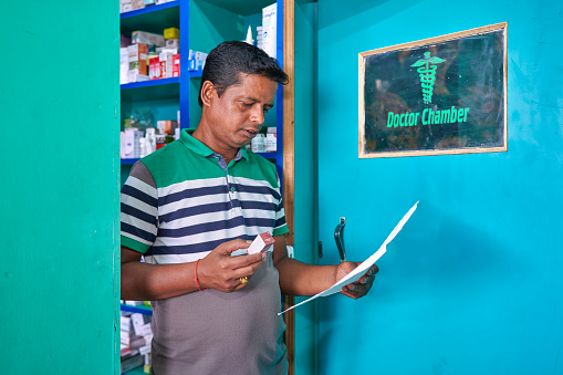 An Indian pharmacist in an Indian pharmacy with a prescription prescribed by a doctor searches for the drug on the pharmacy shelf