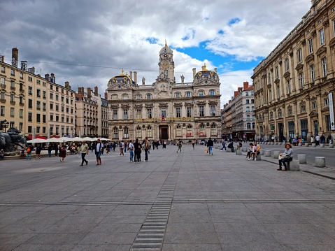 The Place des Terreaux is a square located in the centre of Lyon, France, on the Presqu'île between the Rhône and the Saône rivers, at the foot of the hill of La Croix-Rousse. The image shows the town square capture during autumn season with several people.
