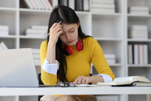 istock Serious Asian female student reading books for exam preparation in university library. 1889686155