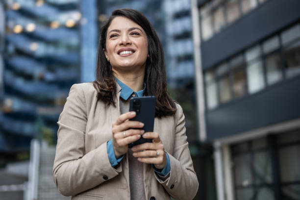 istock Smiling businesswoman reading emails on her mobile phone while on the go 1889696423