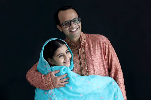 검은 배경에 서 있는 그녀의 아버지와 함께 인도의 전통적인 파란 드레스에서 귀여운 미소 짓는 인도 소녀, 사랑으로 그녀의 아버지를 껴안고 있는 딸 아이. 행복 한 인도 가족, 아이와 함께 아� - men pakistani ethnicity islam malaysian person 뉴스 사진 이미지