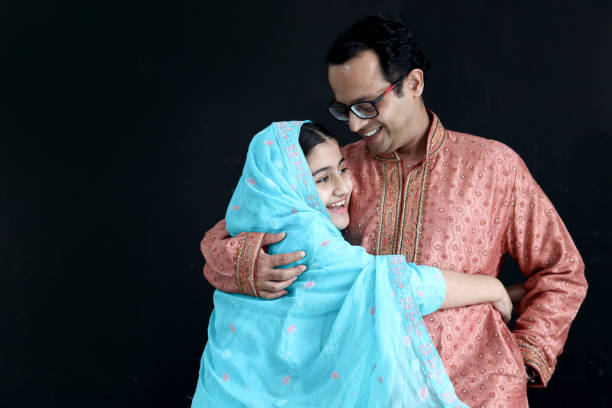 jolie fille indienne souriante en robe bleue traditionnelle indienne avec son père debout sur fond noir, fille enfant étreignant son père avec amour. portrait d’une famille indienne heureuse, père avec enfant. - men pakistani ethnicity islam malaysian person photos et images de collection