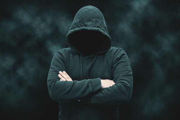 istock Mysterious faceless hooded anonymous criminal, silhouette of computer hacker, cyber terrorist or gangster on black background with smoke 1889707677