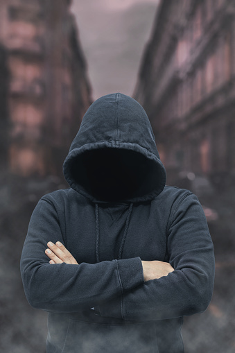 Mysterious faceless hooded anonymous criminal, silhouette of bandit, terrorist or gangster on night city background.
