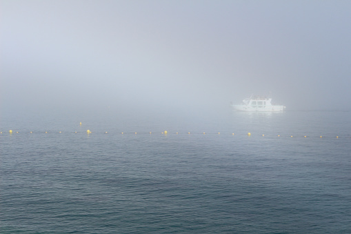 White boat in the mist in the Mediterranean sea, with yellow buoys. Beautiful ray of light. Cassis, Bouches-du-Rhône, France.