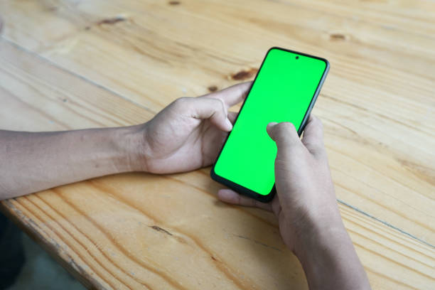 istock A man's hand is operating a smartphone placed on a wooden table with a green screen 1889717084