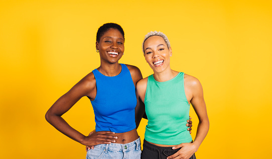 Portrait of a young cheerful female couple in front of a yellow background at studio.Two women together at studio.