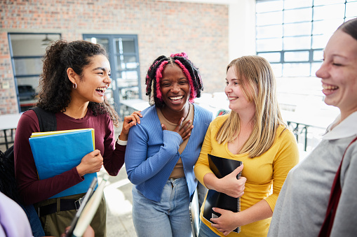 Diverse group of young female college students laughing together while hanging out in a classroom during a break between classes