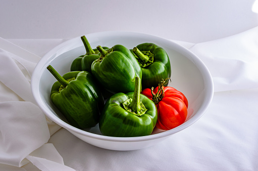 Bowl of green peppers and red heritage tomato in a white bowl on white background