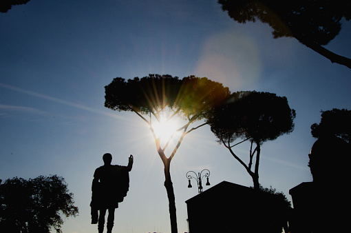 Statue of Roman Emperor in the archeological site of the Imperial Forum in Rome. Sunbeam at sunset over the statue. Rome