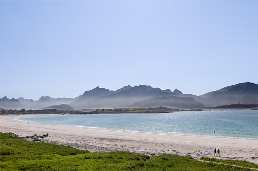 Glistening waters of the North Sea kiss the shores of Jusnesvika Bay Rambergstranda beach in Lofoten, Norway, with a couples strolling and another swimming