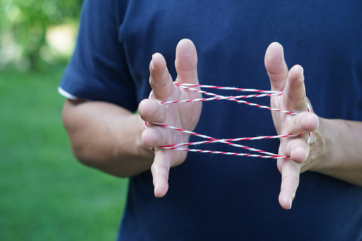 Closeup man hands is playing rope which called cats cradle game. Concept, game involving the creation of various style figures between the fingers. Traditonal playing.