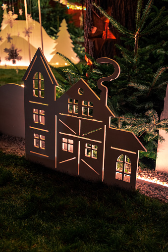 Immortalisez la magie de Noël avec cette image détaillée d'une décoration de Noël artisanale en forme de maison, baignée dans la douce lumière des guirlandes d'un sapin richement décoré, reflétant l'artisanat et les traditions de Strasbourg.