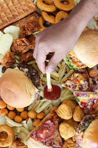 Stock photo showing elevated image of a variety of junk, fast food items including cheeseburgers, chicken burgers, potato waffles, battered onion rings, pizza slices, French fries and a plastic pot of tomato ketchup. Unhealthy eating concept.