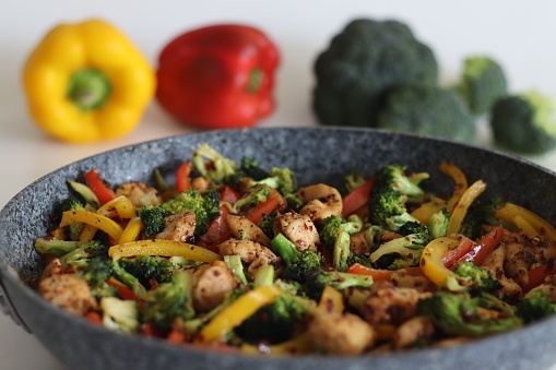 Stir fried vegetables with chicken in frying pan. Air fried chicken cubes tossed with sauteed bell peppers and broccoli. Shot along with broccoli bunches and bell peppers around on white background