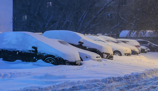 Cars in winter in a parking lot under the snow at night