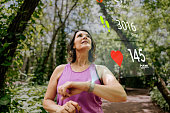 Mature woman with smart watch looking at sports infographic hologram on the public park