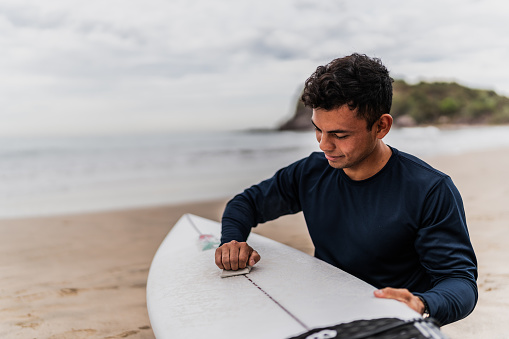 Young surfer man applying paraffin on the surfboard at beach