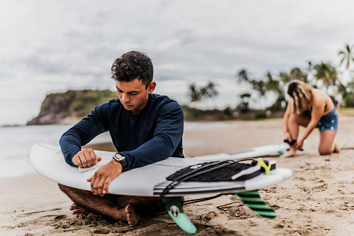 Young surfer man applying paraffin on the surfboard at beach
