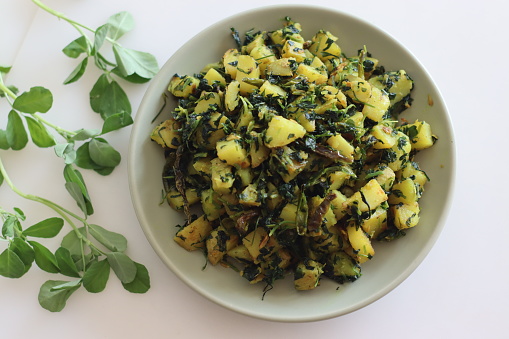 Aloo Methi. A sauteed potato side dish with fresh fragrant fenugreek leaves which is commonly known as methi leaves and spices. Shot on white background