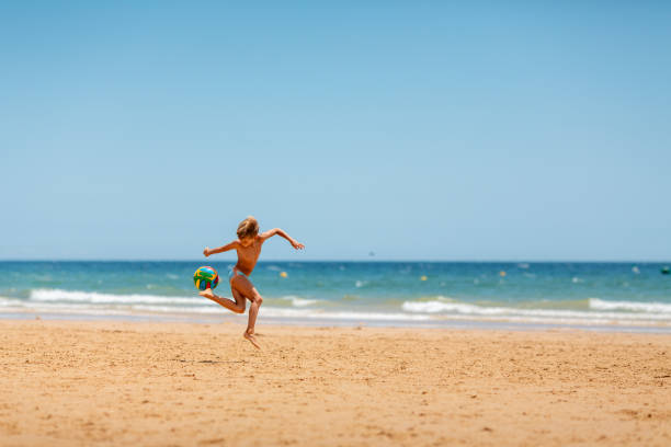 istock Little boy playing with foothball on the beach 1890030591