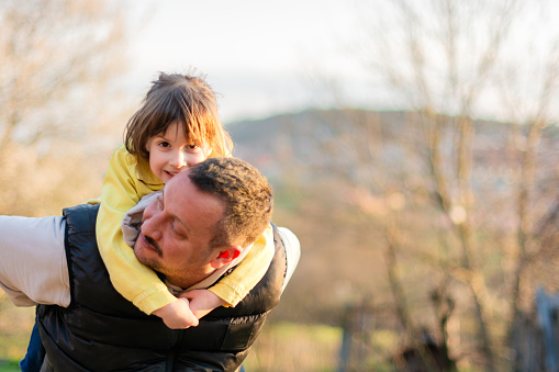 Happy father piggy back his small daughter outdoors.