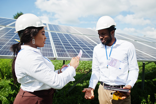 African american technician checks the maintenance of the solar panels. Group of three black engineers meeting at solar station and make a deal with money.