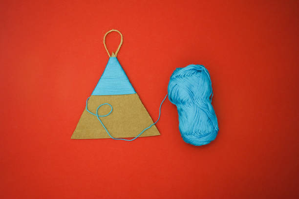 Step by step instructions how to made christmas tree toy a dinosaur of cardboard and threads lies on a red background. The symbol of 2024. Point 3 - wind the thread on the triangle.