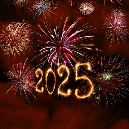 New Year fireworks and 2025 sign made of sparkler trace on a night sky background.