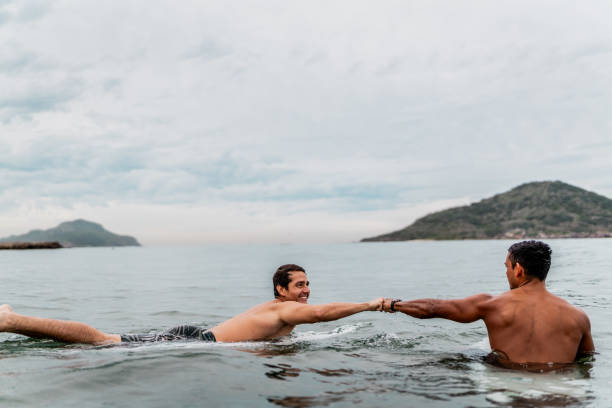 surfer friends bumping fists while surfing on the beach - surfing sport extreme sports success imagens e fotografias de stock