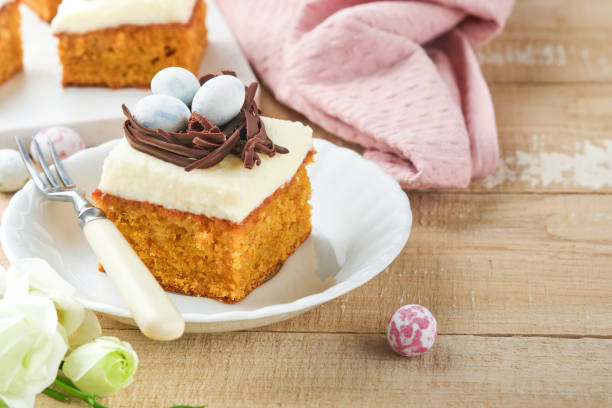 istock Easter carrot cake bars decorated with chocolate nest and chocolate candy eggs blossoming cherry or apple flowers on rustic light wooden backgrounds. Easter holiday meal. Traditional Easter food. 1890141999