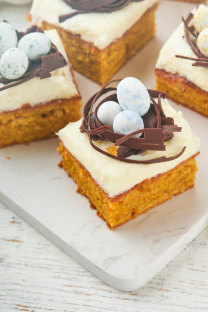 istock Easter carrot cake bars decorated with chocolate nest and chocolate candy eggs blossoming cherry or apple flowers on rustic light wooden backgrounds. Easter holiday meal. Traditional Easter food. 1890142005