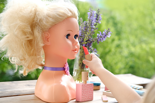 girl's hands imitates painting lips doll, playing with set of stylist, beautician in garden, on balcony, simulation games in profession, training girls in art of makeup artist